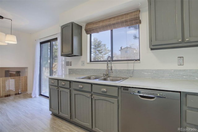 kitchen with pendant lighting, sink, gray cabinets, stainless steel dishwasher, and light wood-type flooring