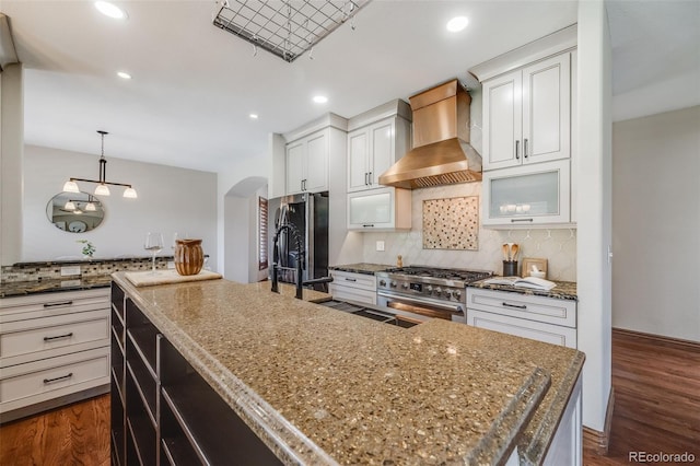 17522 E Dewberry Dr, Parker, CO 80134 - kitchen featuring wall chimney range hood, stainless steel range, arched walkways, freestanding refrigerator, and decorative backsplash