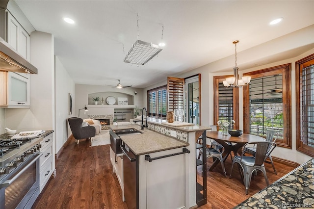 17522 E Dewberry Dr, Parker, CO 80134 - kitchen with stainless steel stove, a lit fireplace, wall chimney range hood, dark wood-type flooring, and recessed lighting