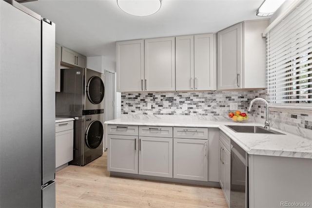 4728 Dover St, Wheat Ridge, CO 80033 - kitchen featuring stacked washing machine and dryer, gray cabinets, appliances with stainless steel finishes, decorative backsplash, and light wood-type flooring