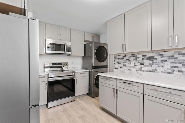 4728 Dover St, Wheat Ridge, CO 80033 - kitchen with appliances with stainless steel finishes, stacked washer / dryer, light wood-style flooring, decorative backsplash, and light stone counters