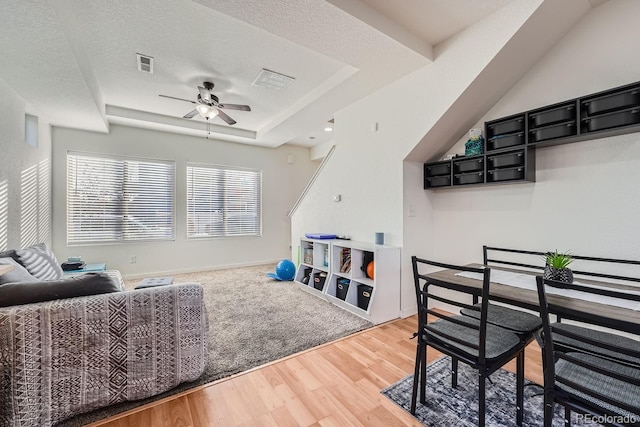 living room featuring wood-type flooring, a textured ceiling, a tray ceiling, and ceiling fan