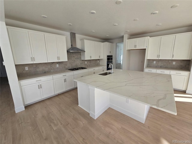 kitchen with wall chimney exhaust hood, a sink, a large island with sink, and light wood-style floors