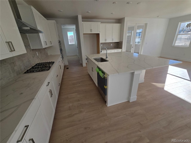 kitchen with light wood finished floors, white cabinets, wall chimney exhaust hood, appliances with stainless steel finishes, and a sink