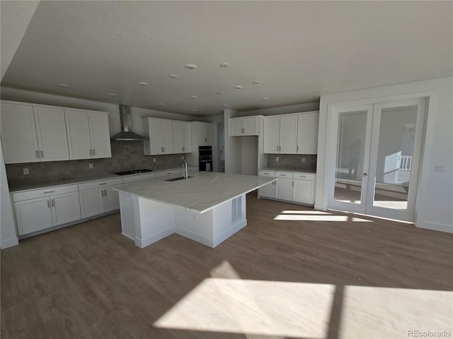 kitchen featuring wood finished floors, a sink, white cabinets, wall chimney range hood, and black appliances