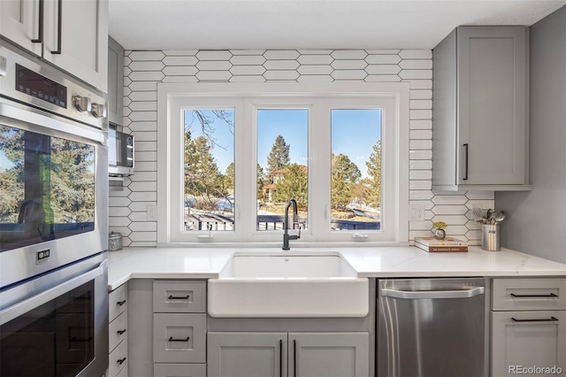 kitchen with gray cabinets, appliances with stainless steel finishes, sink, decorative backsplash, and light stone counters