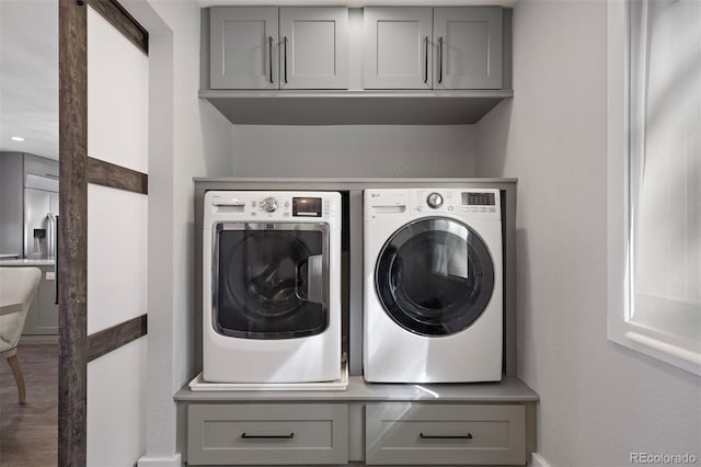 clothes washing area with cabinets, wood-type flooring, and washer and dryer