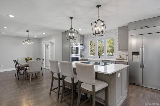 kitchen featuring a kitchen island, appliances with stainless steel finishes, gray cabinetry, light countertops, and an inviting chandelier