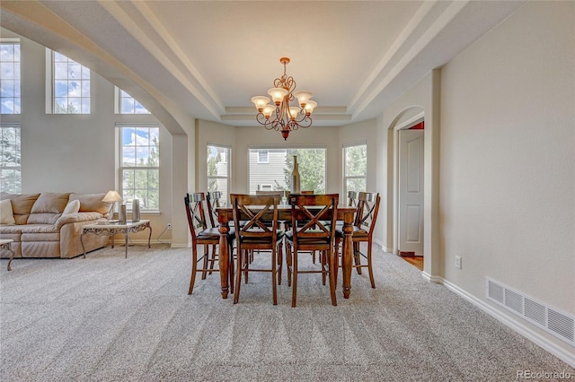 carpeted dining space with a tray ceiling and a chandelier