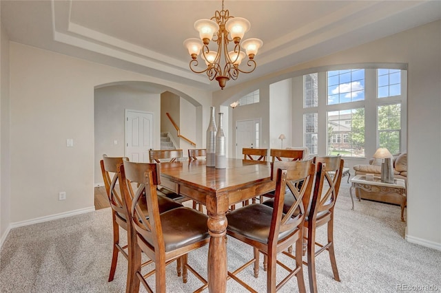 dining room featuring a raised ceiling, light colored carpet, and a notable chandelier