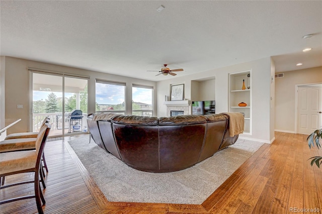 living room featuring ceiling fan, light wood-type flooring, built in features, and a textured ceiling