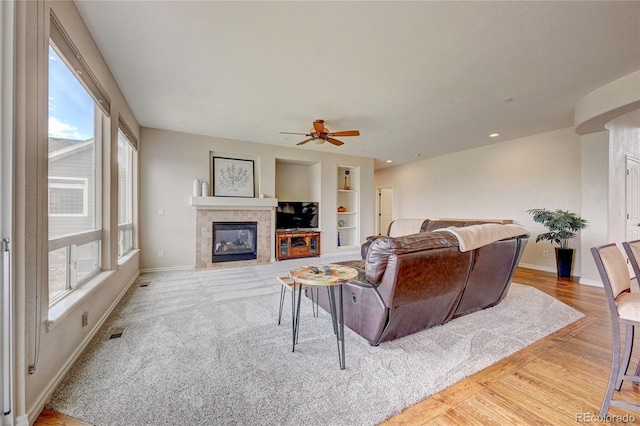 living room featuring a tile fireplace, built in shelves, ceiling fan, and a healthy amount of sunlight