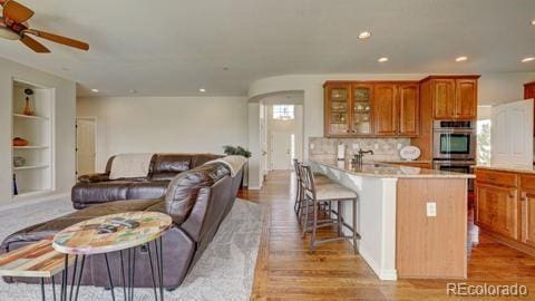 kitchen featuring ceiling fan, built in features, light wood-type flooring, stainless steel double oven, and a breakfast bar area