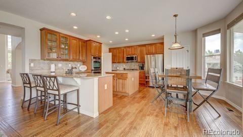 kitchen with a breakfast bar, light wood-type flooring, decorative light fixtures, kitchen peninsula, and stainless steel appliances