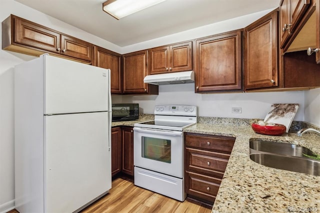 kitchen featuring under cabinet range hood, white appliances, a sink, light wood-style floors, and light stone countertops