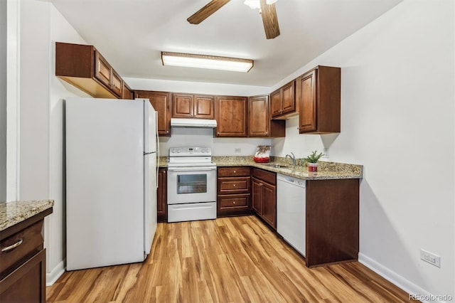 kitchen featuring light wood finished floors, a sink, light stone countertops, white appliances, and under cabinet range hood