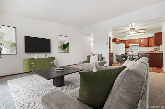 living area with light carpet, ceiling fan, and baseboards