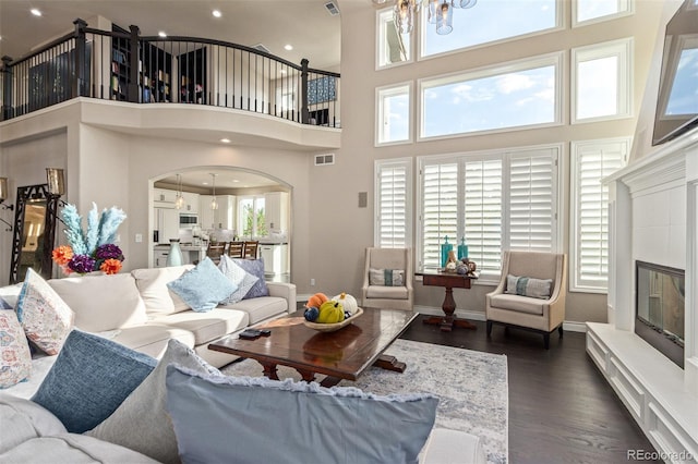 618 Fairchild Dr, Highlands Ranch, CO 80126 - living room with arched walkways, a towering ceiling, a tiled fireplace, dark wood-style flooring, and visible vents