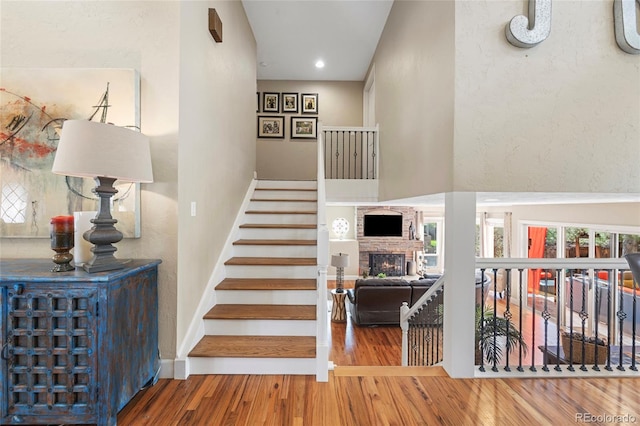 stairs featuring a healthy amount of sunlight, hardwood / wood-style floors, and a stone fireplace