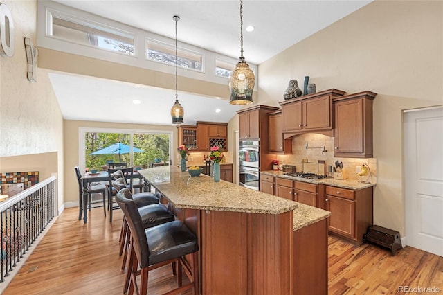 kitchen featuring hanging light fixtures, light hardwood / wood-style flooring, appliances with stainless steel finishes, light stone counters, and decorative backsplash