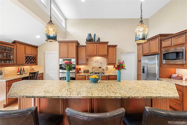 kitchen with light stone countertops, pendant lighting, backsplash, appliances with stainless steel finishes, and a breakfast bar