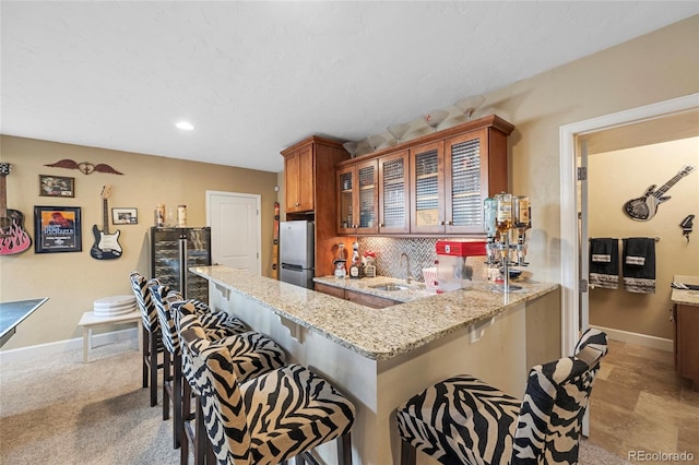 kitchen with light stone countertops, sink, stainless steel fridge, kitchen peninsula, and a breakfast bar