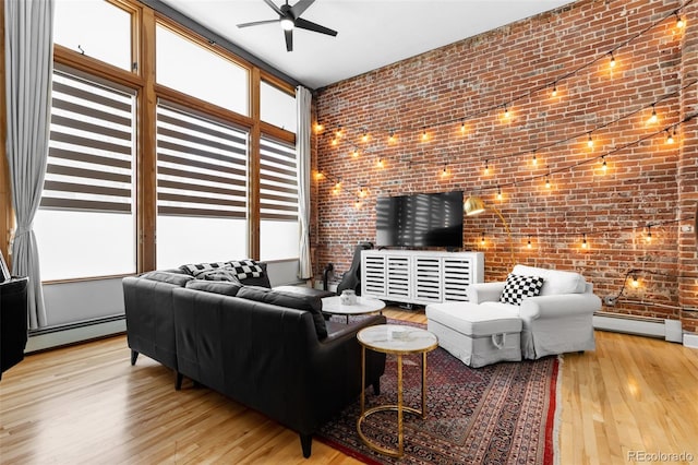 living room featuring light wood-type flooring, a high ceiling, brick wall, and a baseboard radiator