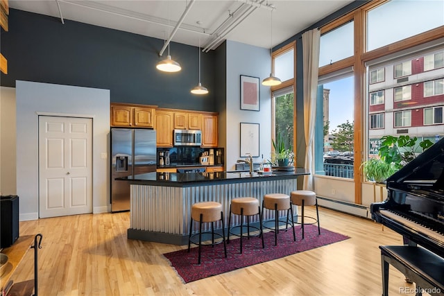 kitchen featuring a high ceiling, a baseboard heating unit, a kitchen breakfast bar, light hardwood / wood-style floors, and stainless steel appliances