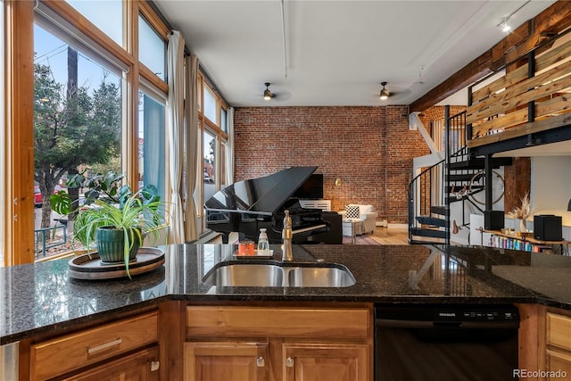 kitchen featuring dark stone countertops, sink, brick wall, and black dishwasher