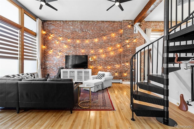 living room with ceiling fan, a baseboard radiator, beam ceiling, wood-type flooring, and brick wall