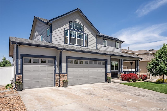 view of front of home featuring a porch, driveway, an attached garage, stone siding, and fence