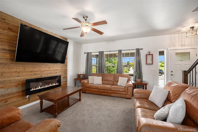 carpeted living room featuring a ceiling fan, a glass covered fireplace, and stairs