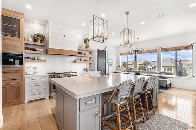 7033 E Lake Cir, Centennial, CO 80111 - kitchen featuring stainless steel gas stove, a kitchen bar, open shelves, light wood-style floors, and a kitchen island with sink