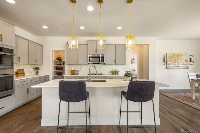 kitchen with dark hardwood / wood-style floors, a center island with sink, pendant lighting, and appliances with stainless steel finishes