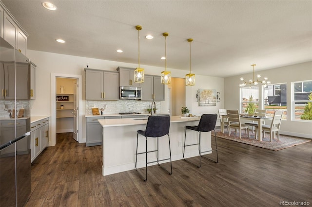 kitchen featuring dark hardwood / wood-style floors, backsplash, a notable chandelier, appliances with stainless steel finishes, and pendant lighting