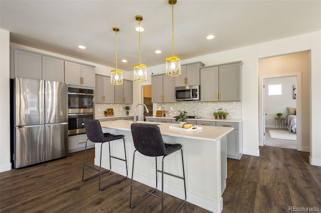 kitchen with appliances with stainless steel finishes, decorative light fixtures, a center island with sink, and dark hardwood / wood-style flooring