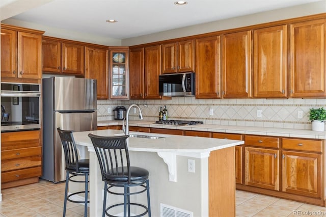 kitchen featuring visible vents, brown cabinets, a sink, stainless steel appliances, and light countertops