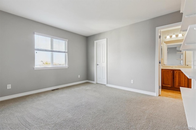 unfurnished bedroom featuring visible vents, baseboards, light colored carpet, and ensuite bathroom