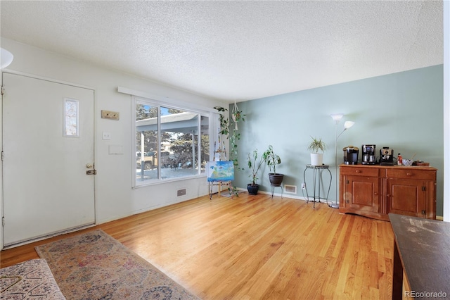 entryway featuring light wood-style flooring, baseboards, visible vents, and a textured ceiling