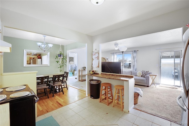 living room with a wealth of natural light, ceiling fan with notable chandelier, light carpet, and light tile patterned floors