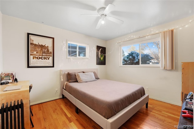 bedroom featuring radiator heating unit, a ceiling fan, baseboards, and light wood finished floors