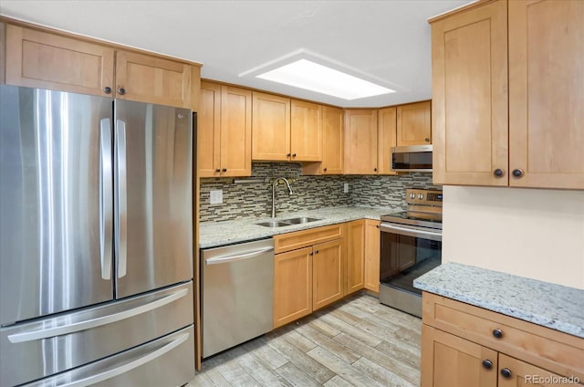 kitchen featuring stainless steel appliances, a sink, light wood-type flooring, backsplash, and light stone countertops
