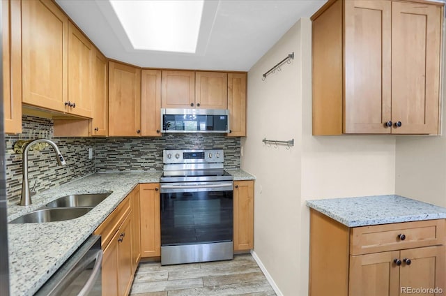 kitchen featuring stainless steel appliances, a sink, light wood finished floors, backsplash, and light stone countertops