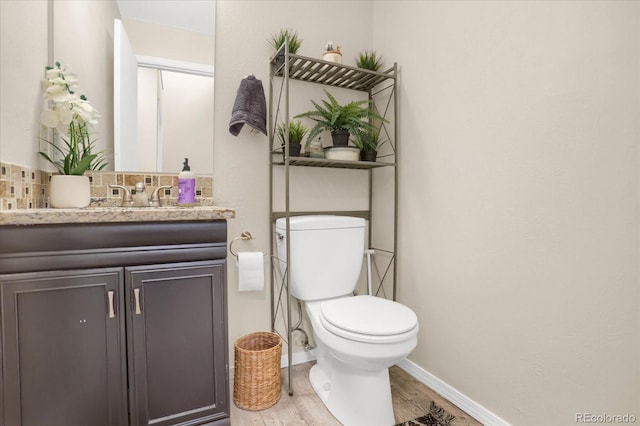 bathroom with wood finished floors, baseboards, vanity, toilet, and backsplash