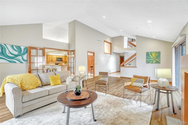 living room with high vaulted ceiling, plenty of natural light, a textured ceiling, and light hardwood / wood-style floors