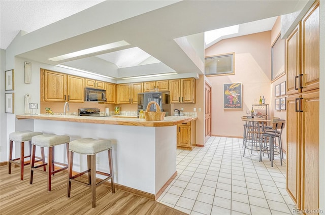 kitchen featuring a kitchen bar, kitchen peninsula, stainless steel appliances, light wood-type flooring, and vaulted ceiling