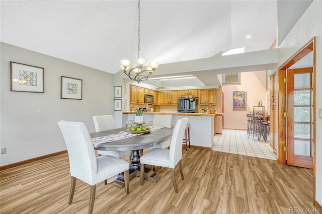 dining space with light wood-type flooring, a notable chandelier, and vaulted ceiling