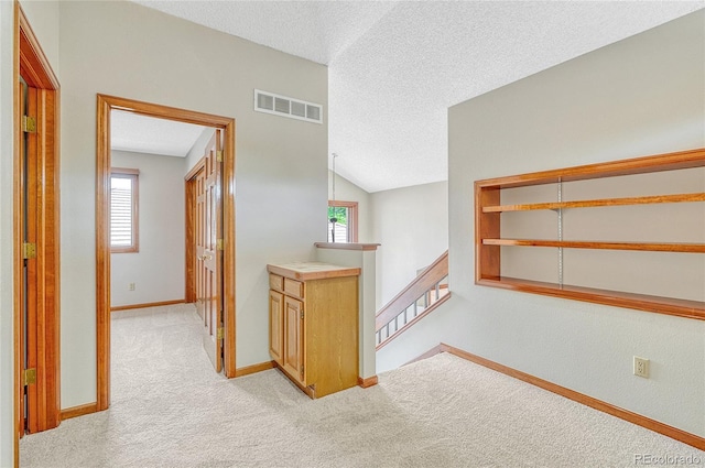 hallway featuring lofted ceiling, light colored carpet, a wealth of natural light, and a textured ceiling