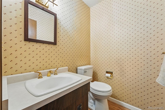 1354 S Macon St, Aurora, CO 80012 - half bathroom with wallpapered walls, toilet, vanity, baseboards, and wood finished floors