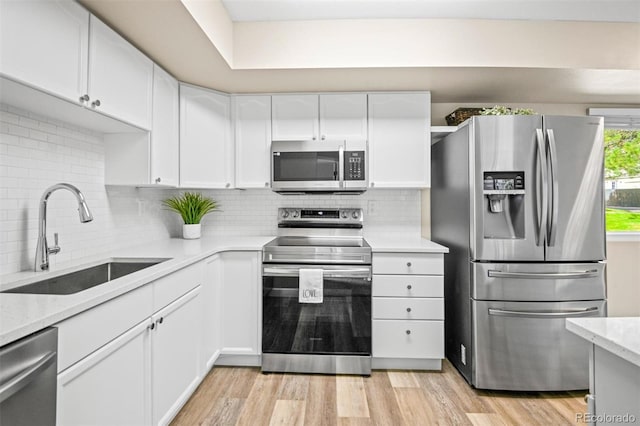 kitchen featuring sink, light hardwood / wood-style flooring, backsplash, white cabinets, and appliances with stainless steel finishes